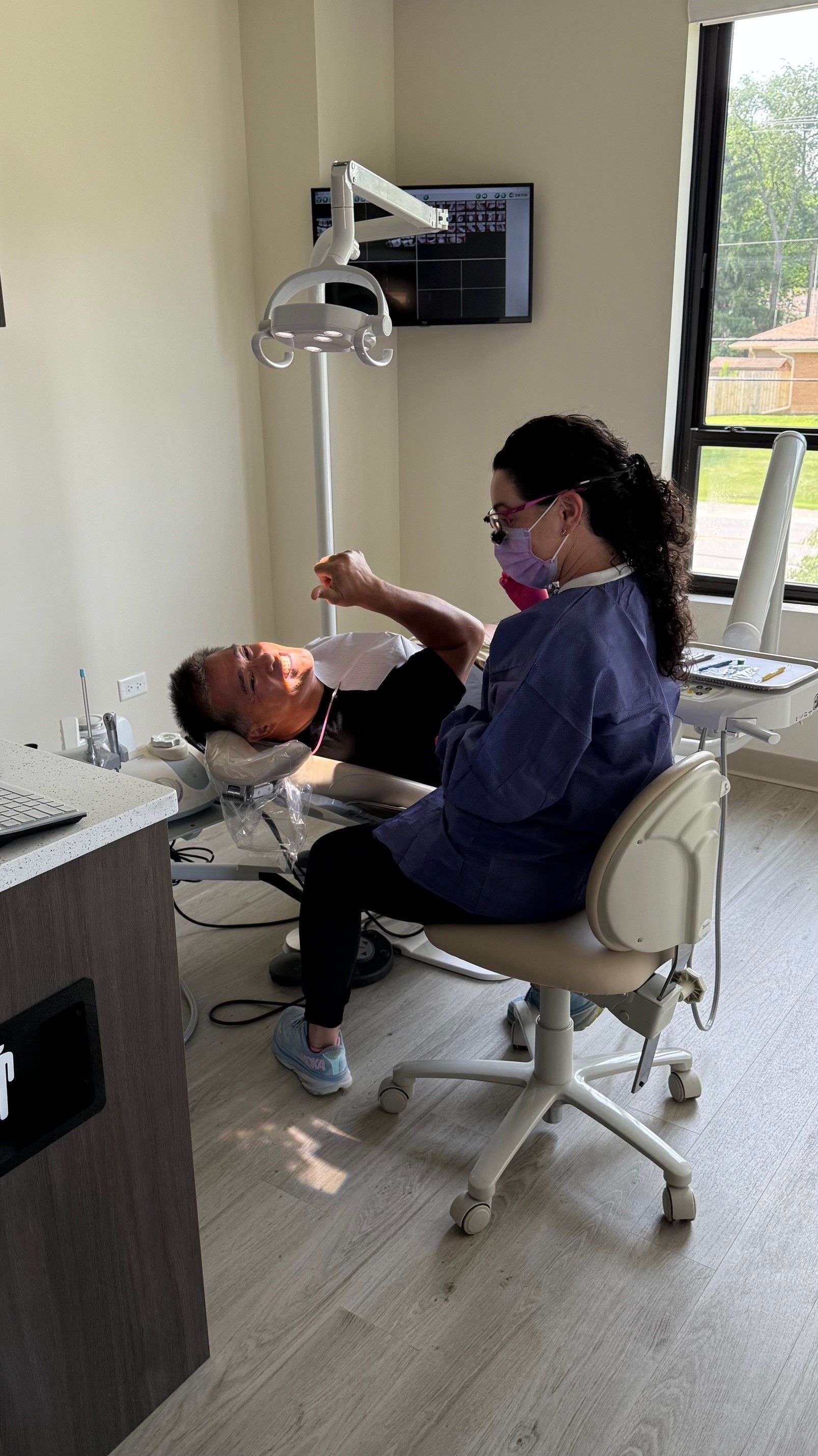 Dentist examining a patient's mouth in a dental office. The dentist is wearing a mask and scrubs.