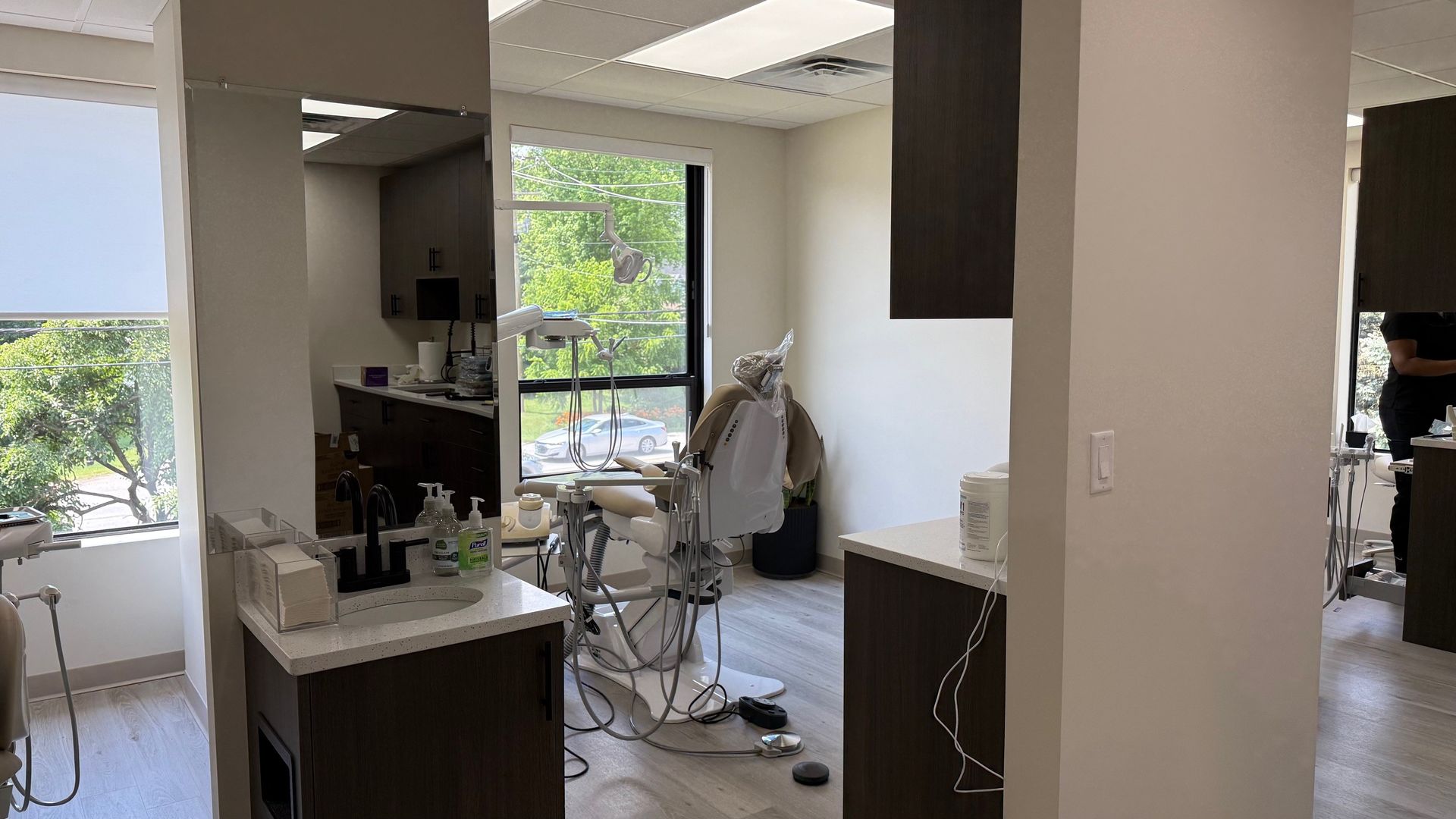 Dental office room, white walls, dental chair, window with outdoor view, cabinets, and mirrors.