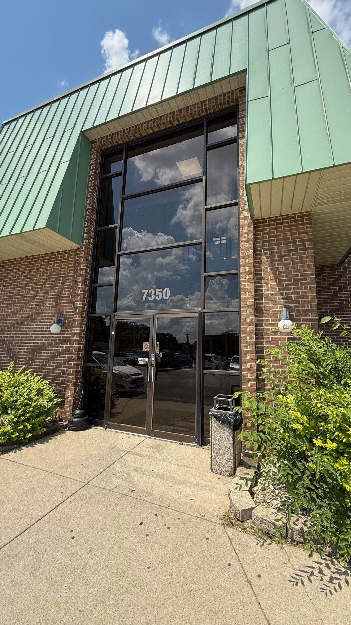 Entrance to a building with black-framed glass doors and windows, brick exterior, and green roof. Address 3350 visible.