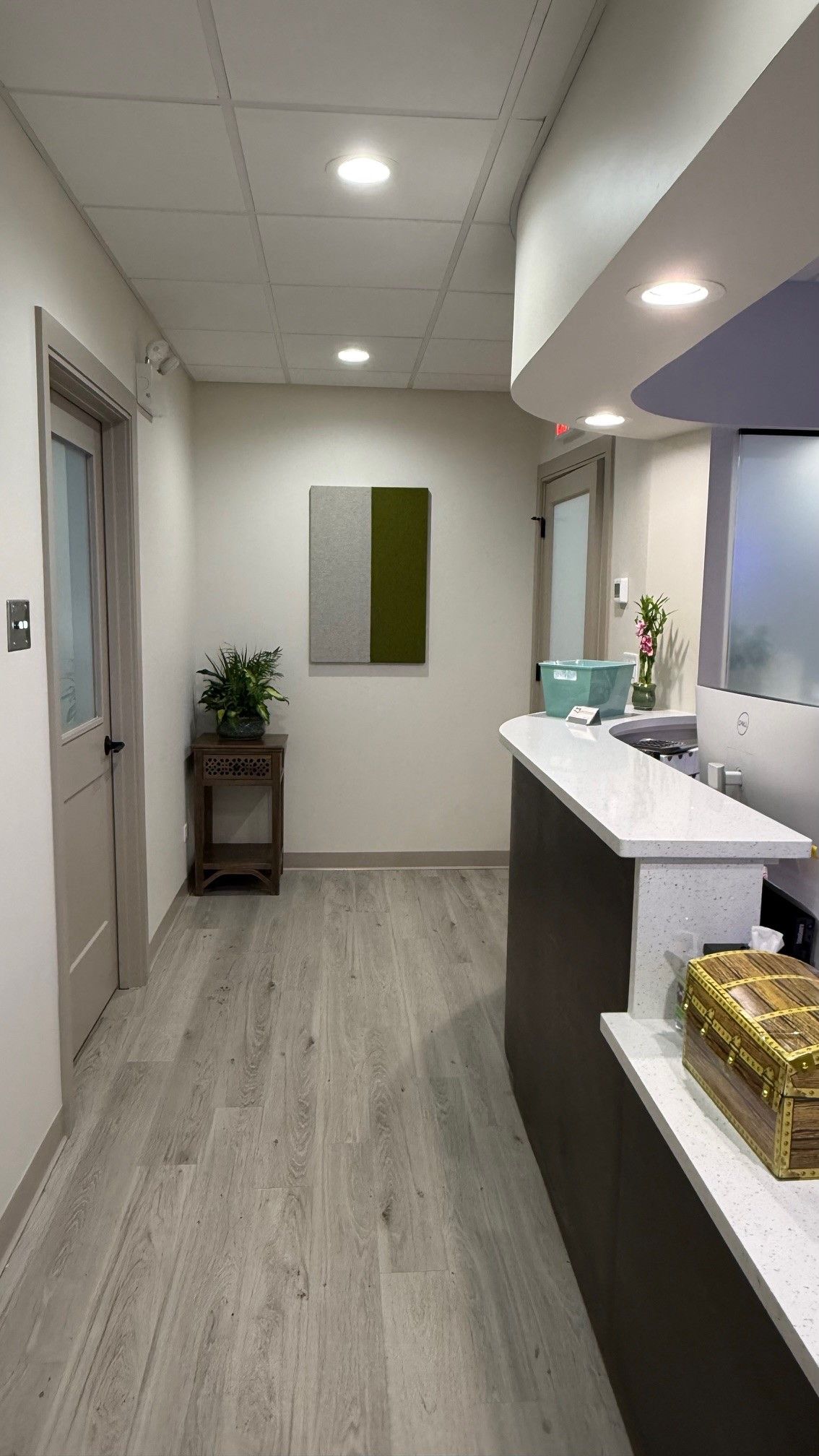 Reception area with a desk, hallway, artwork, and wood-like flooring.