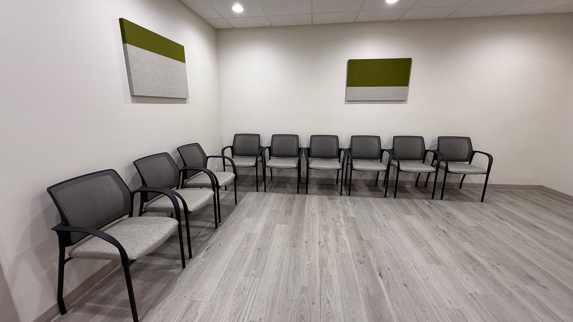 Waiting room with rows of gray chairs, white walls, and abstract art.