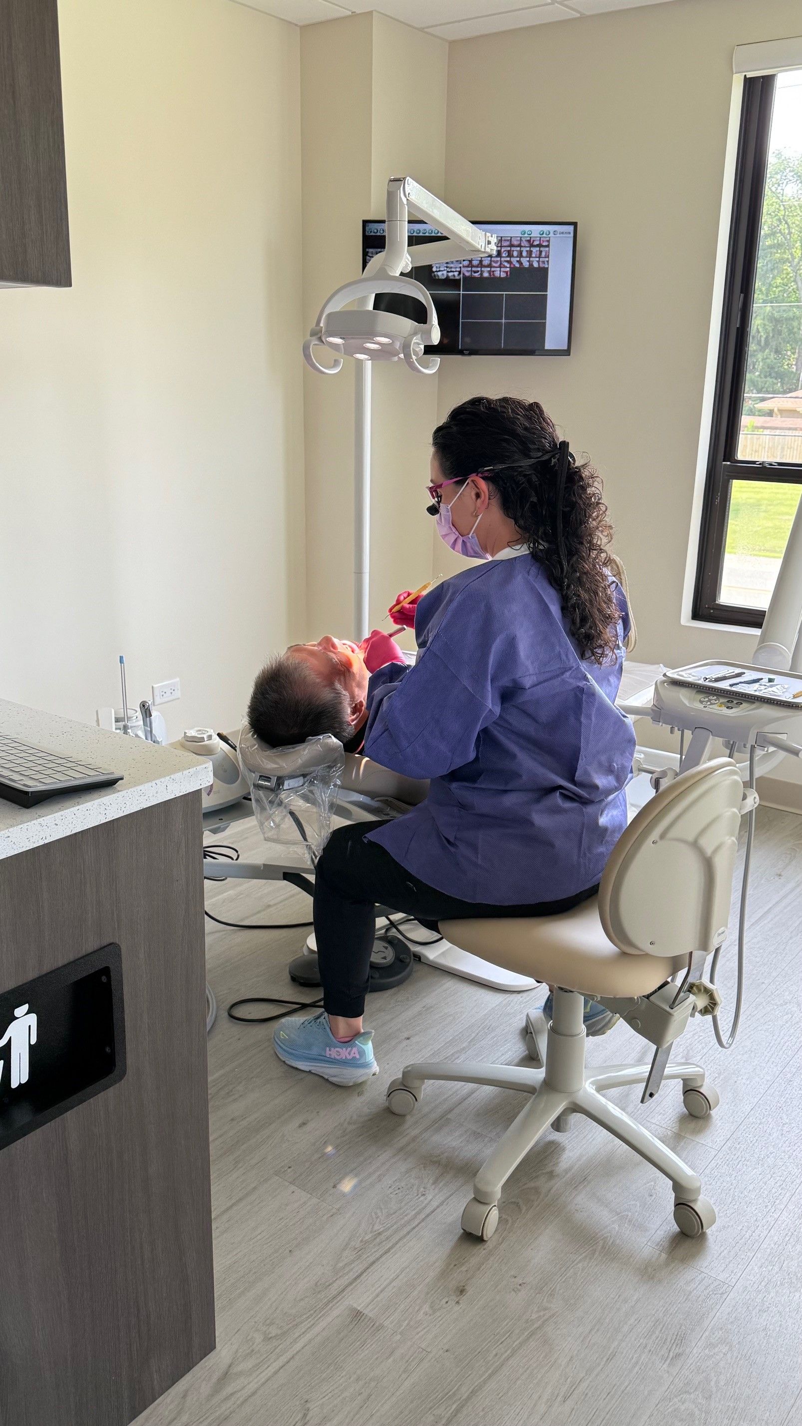 Dentist examining a patient in a dental office. The dentist is wearing scrubs and a mask.