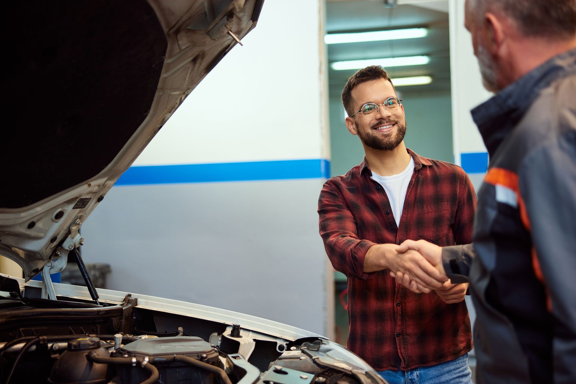 Man shaking hands with a uniformed mechanic with a car hood opened.