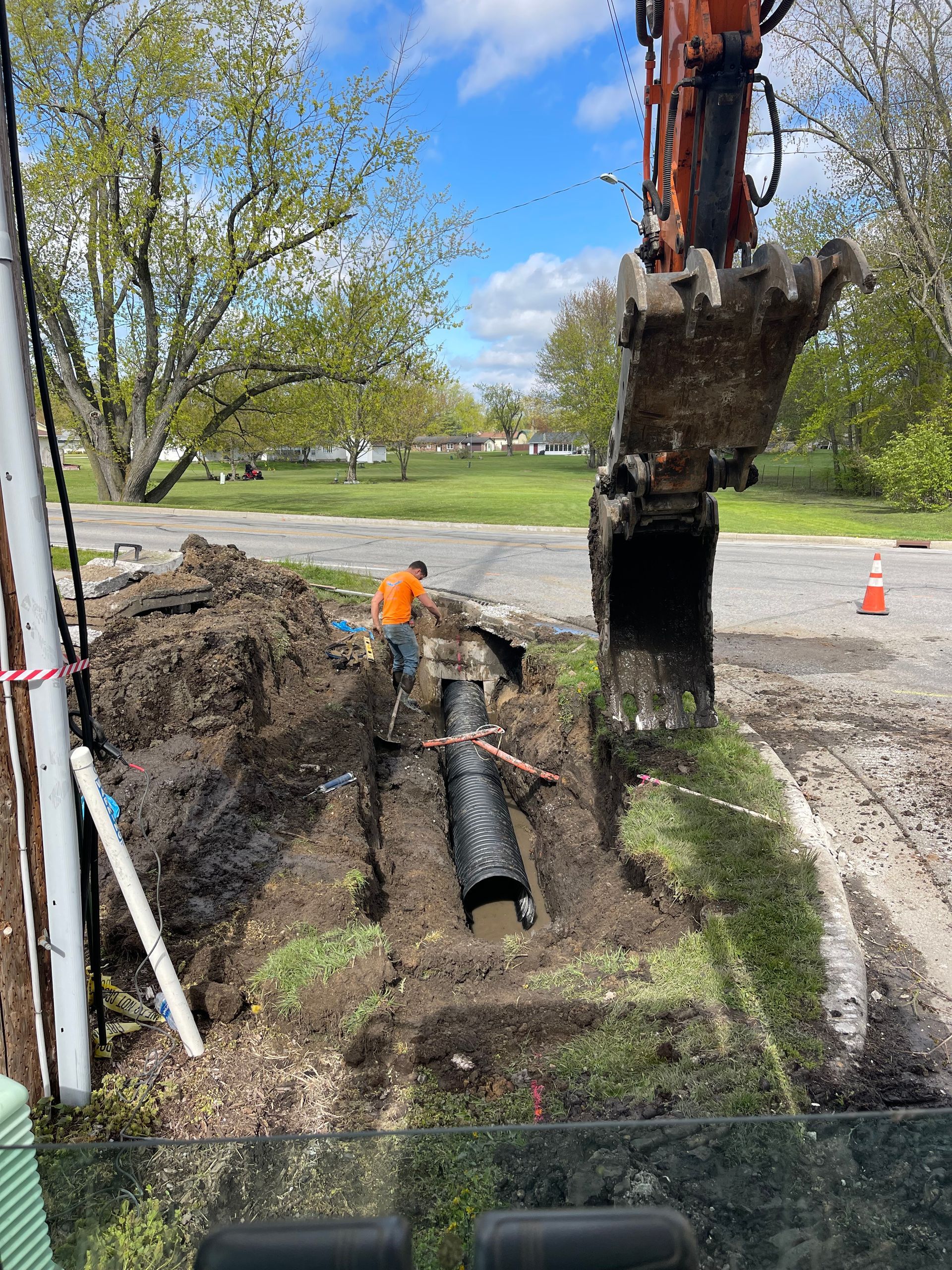 Pipeline construction in a forest. Black pipe next to a trench being dug by an excavator.