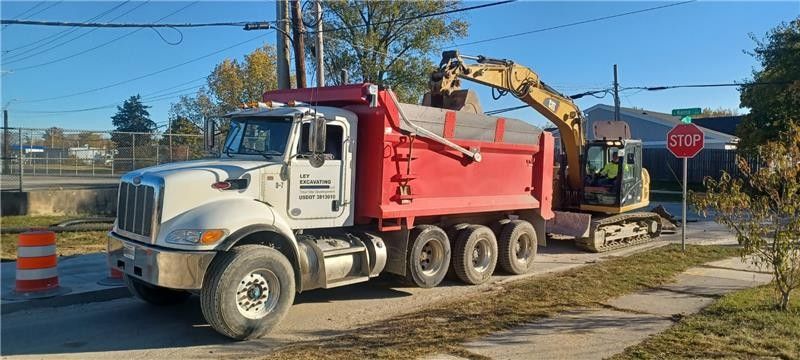 Heavy machinery loading a dump truck at a quarry, with piles of sand and rock.