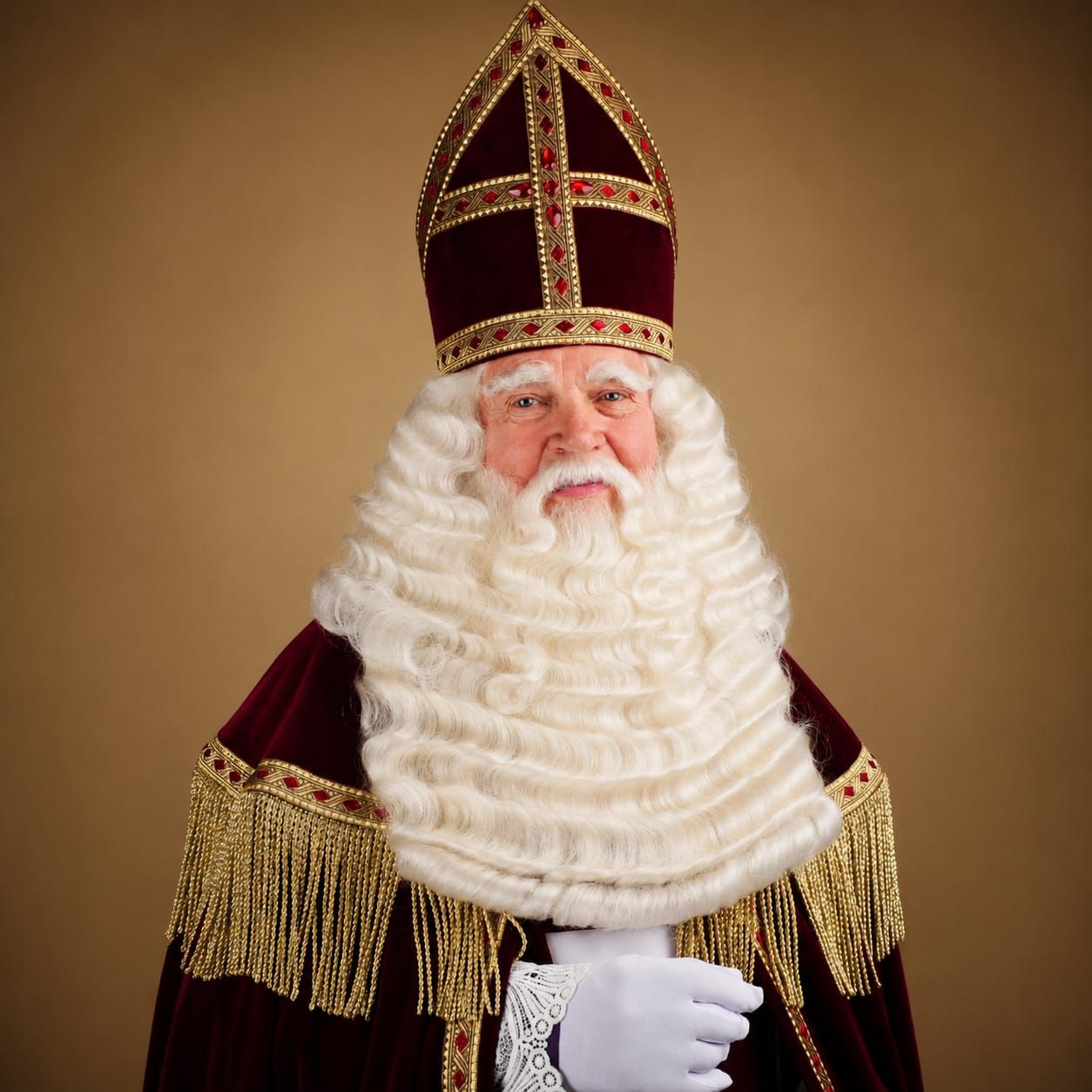 sint in een rood fluwelen pak met gouden versieringen en een lange witte baard, staand tegen een warme bruine achtergrond.