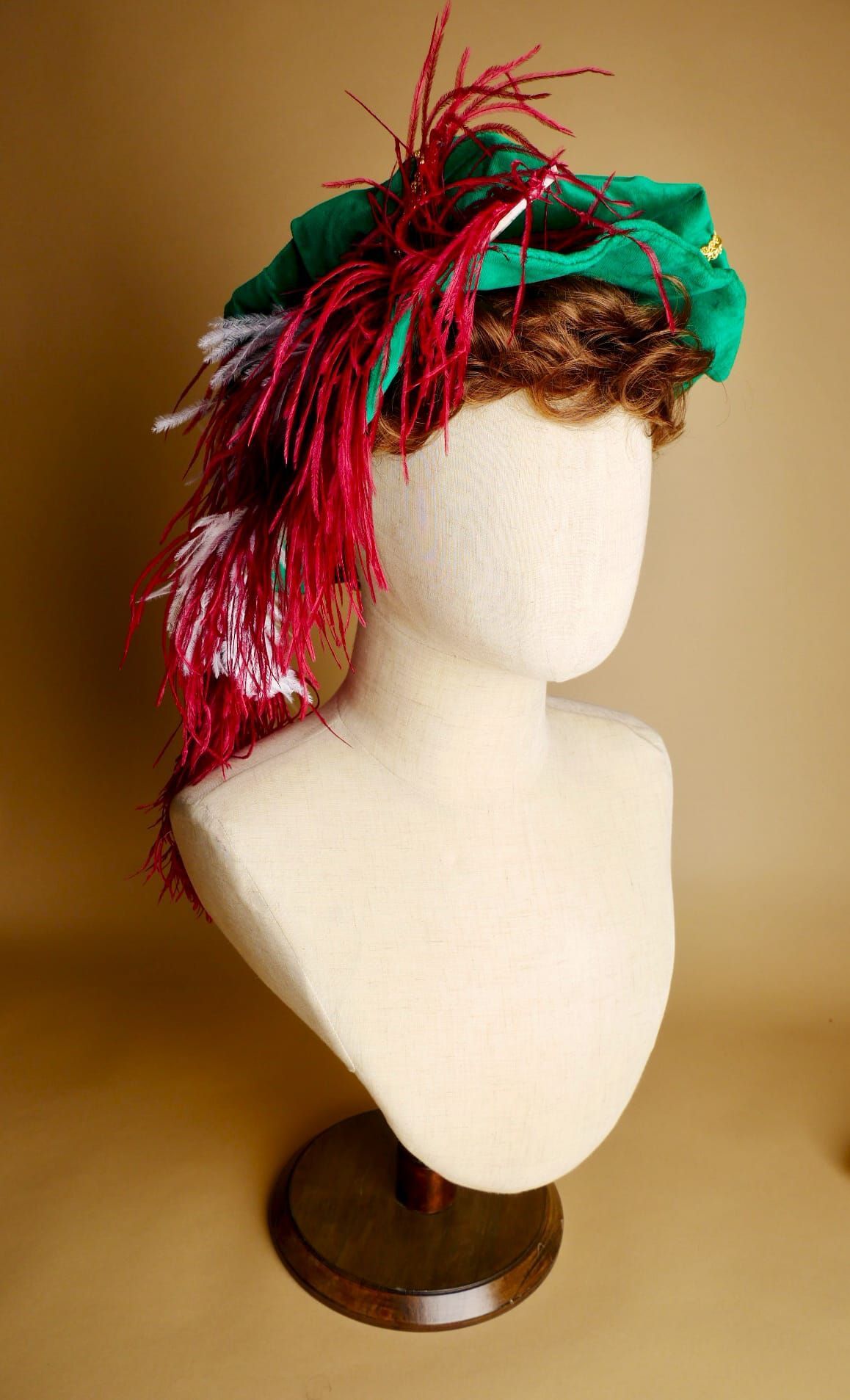 Mannequinhoofd met groene hoed, rode en witte veren, bruine voet.
