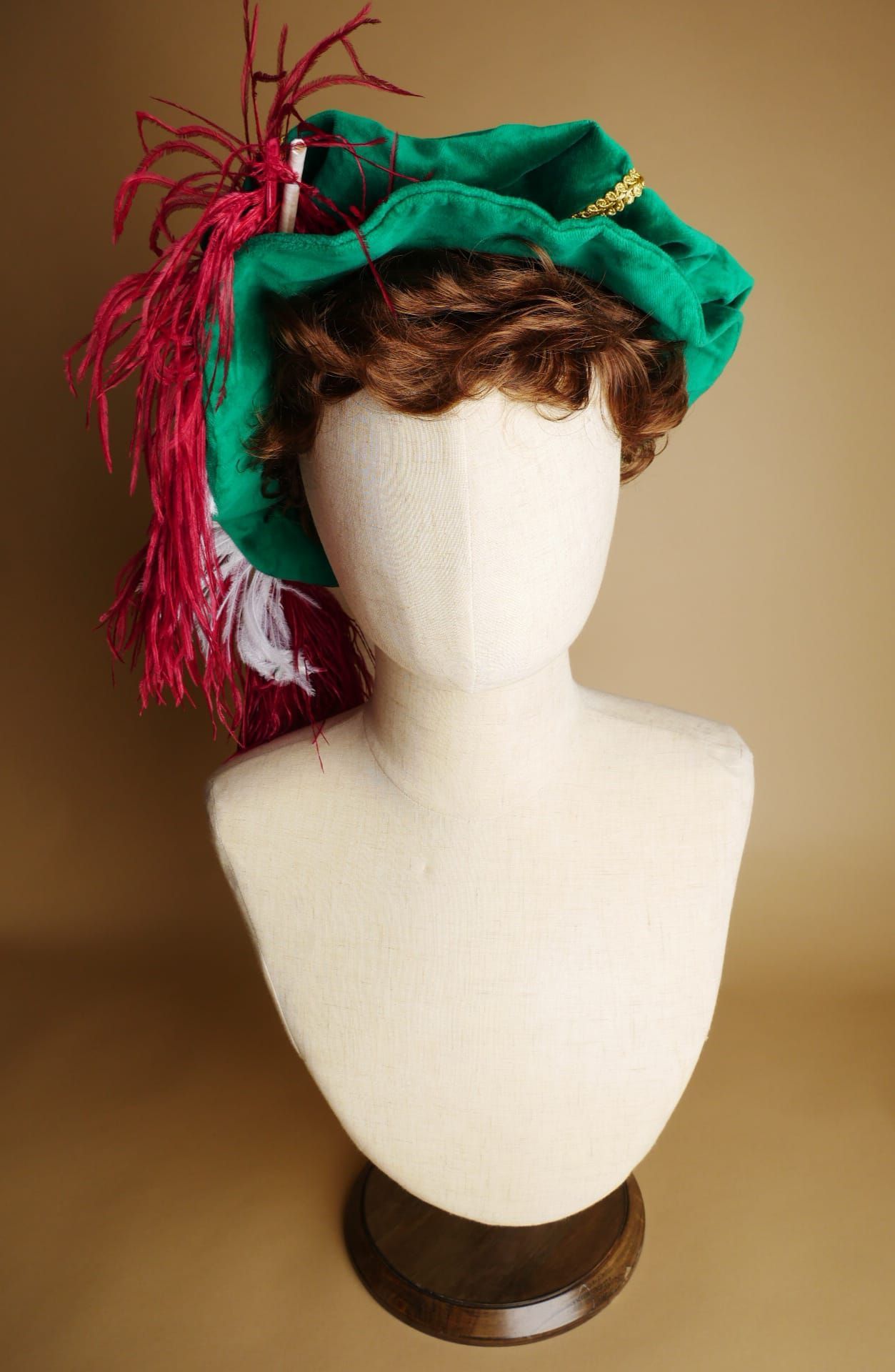 Mannequinhoofd met groene hoed, rode en witte veren, bruine voet.