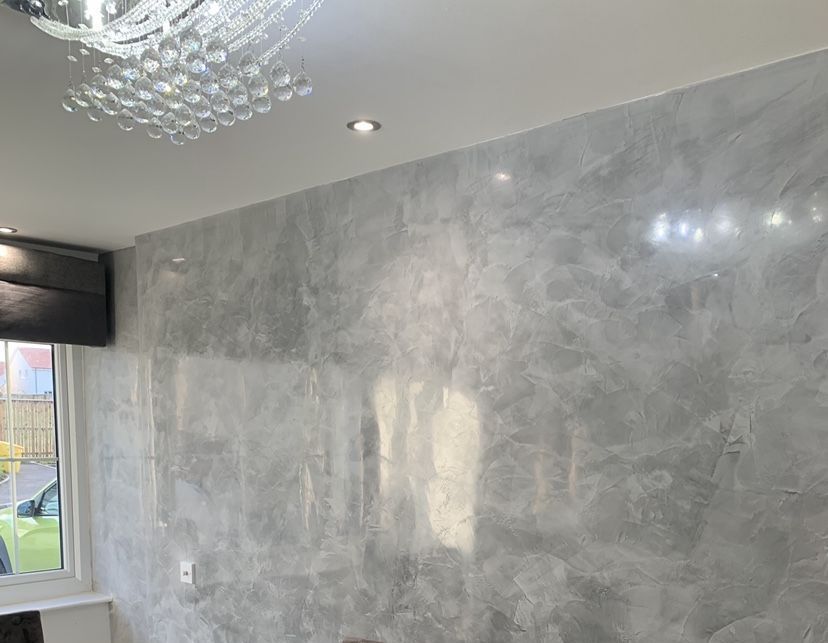 Close-up of a textured Venetian plaster wall in shades of black and gray, showcasing a blend of smooth and rough surfaces with subtle variations in color and light reflections.