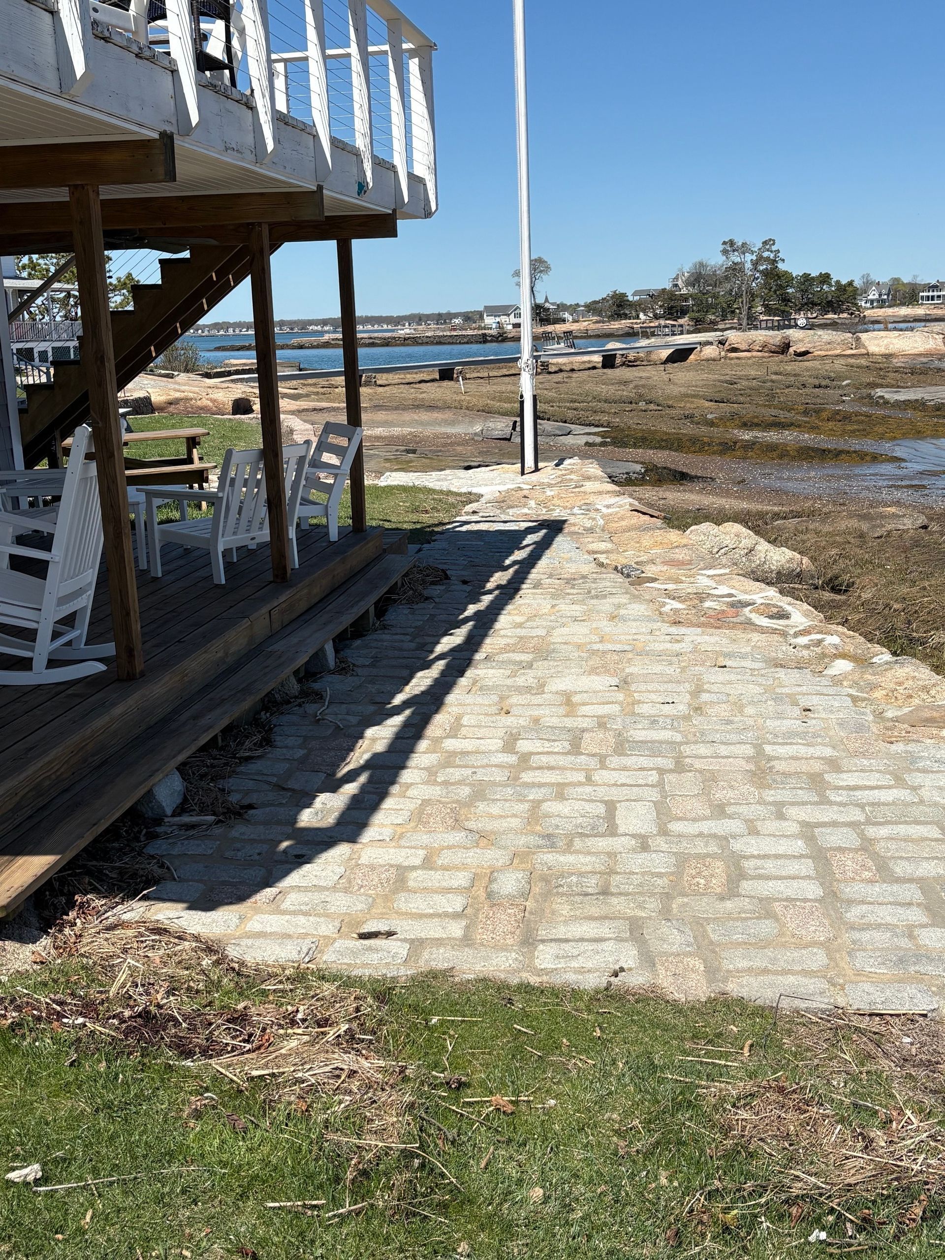 Stone walkway beside a raised deck, leading toward a rocky shoreline under a clear blue sky.