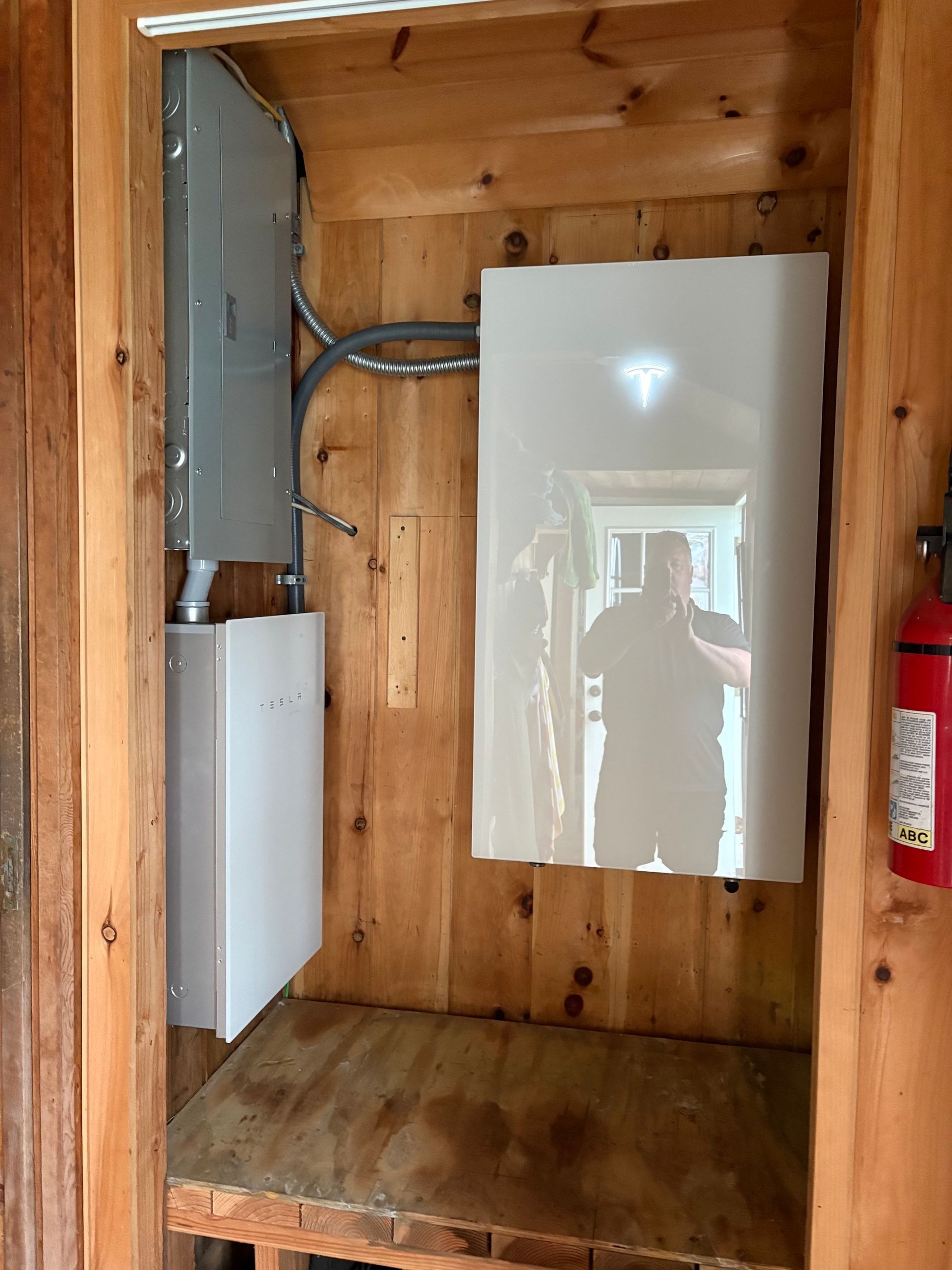 Wooden utility closet with electrical panels and a fire extinguisher mounted on the right wall