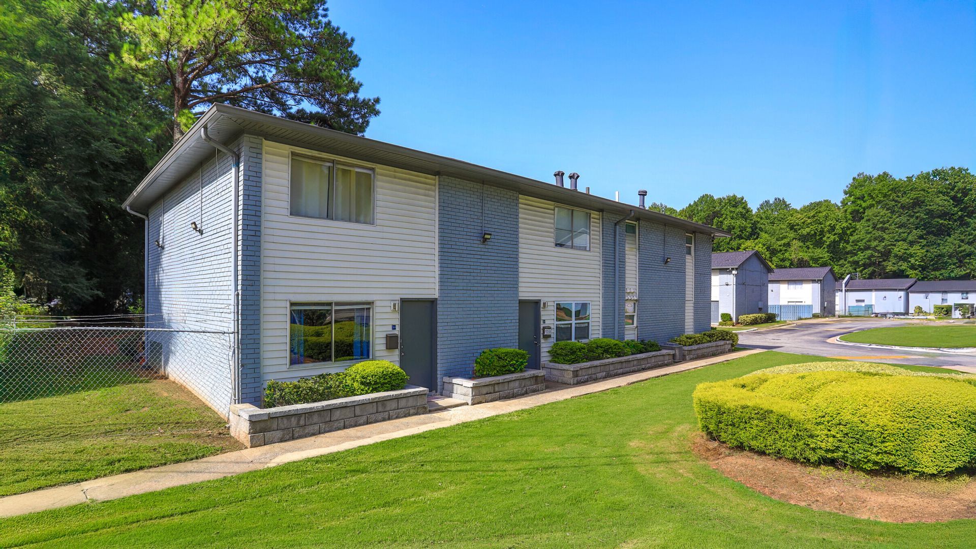 Apartment building with light gray siding, blue shutters, and green lawn on a sunny day