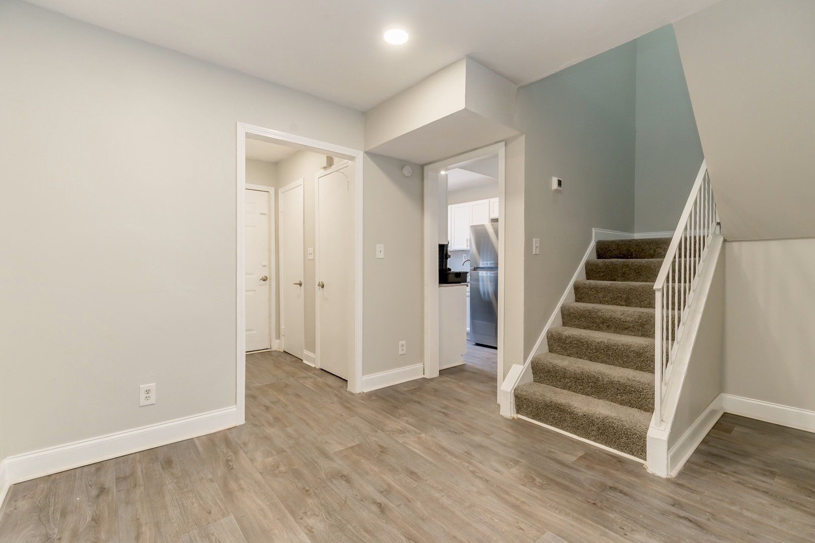 Empty entryway with wood floors, white walls, closet doors, and carpeted stairs leading up.