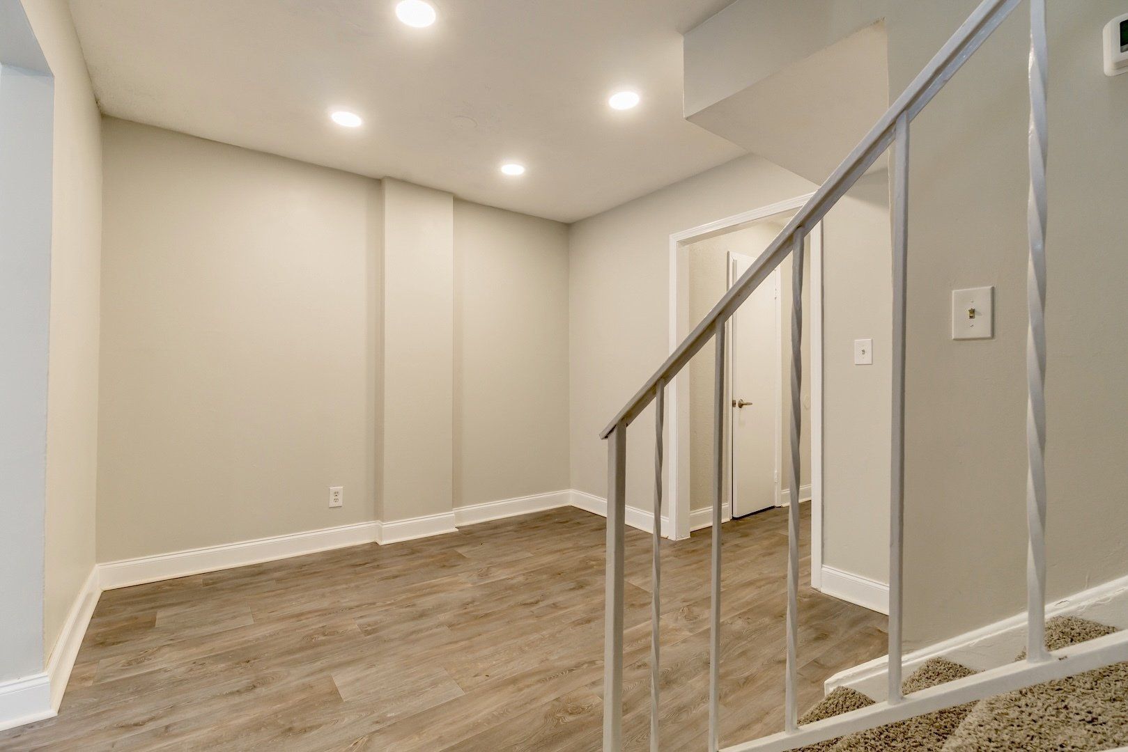 Empty finished basement with recessed lights, wood-look flooring, and a staircase railing in the foreground