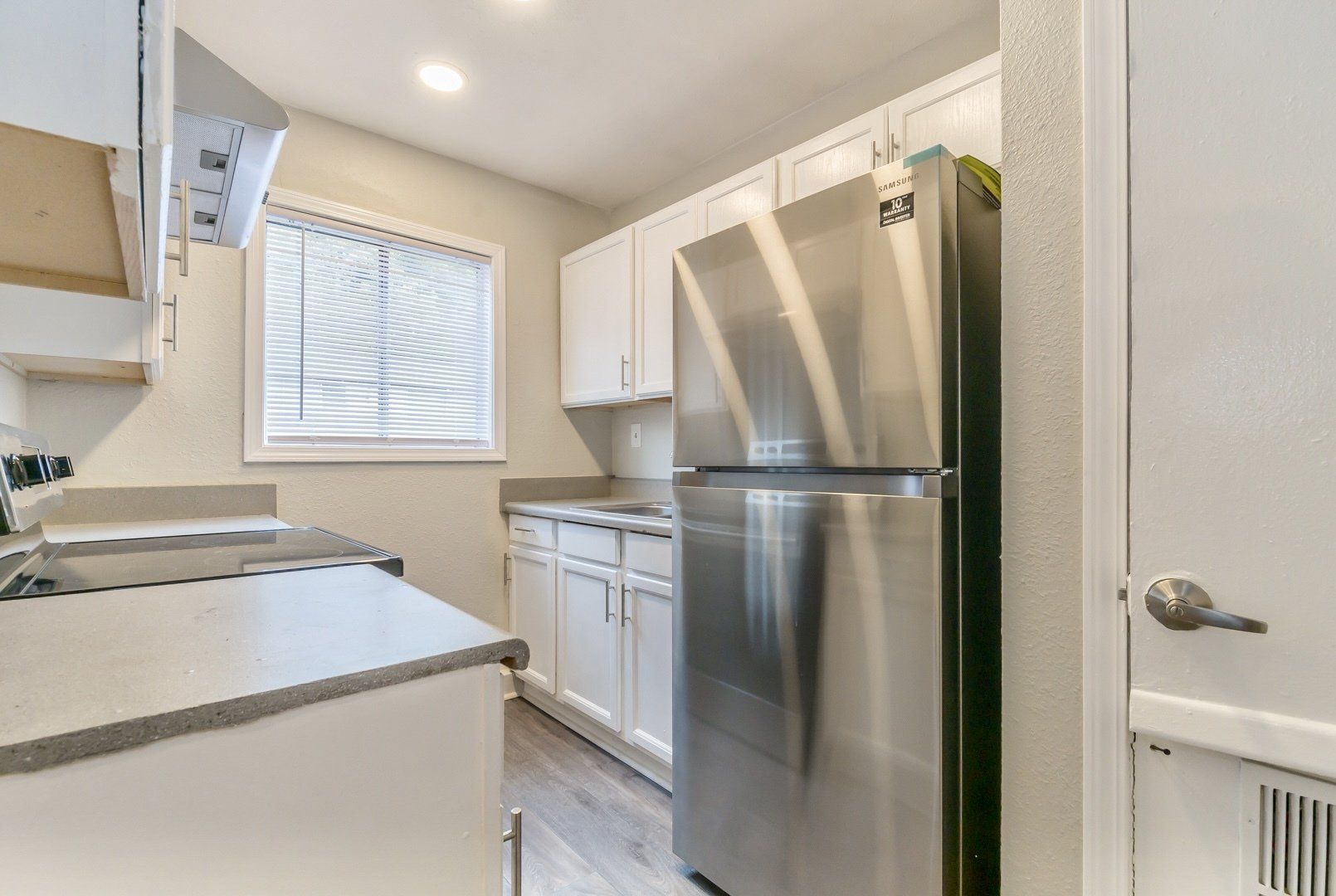 Bright galley kitchen with white cabinets, stainless steel fridge, and a window over the sink.