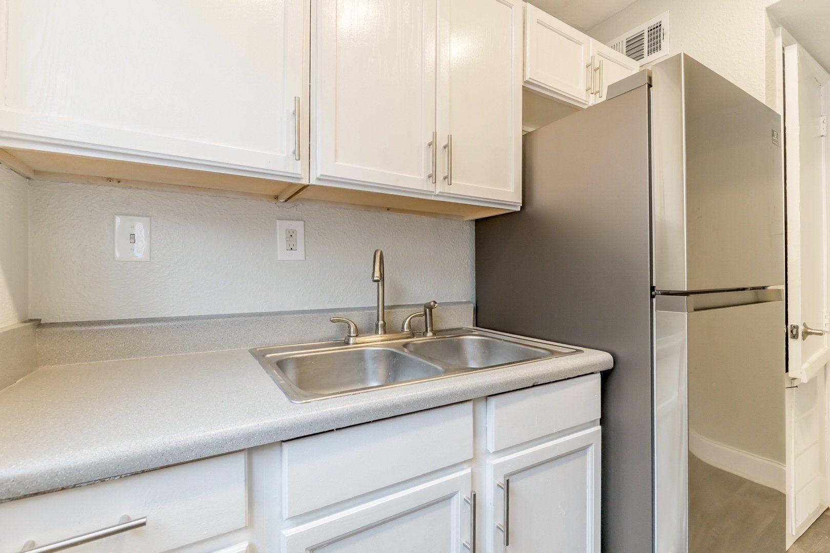 Small kitchen with white cabinets, sink, and a stainless steel refrigerator by an open door