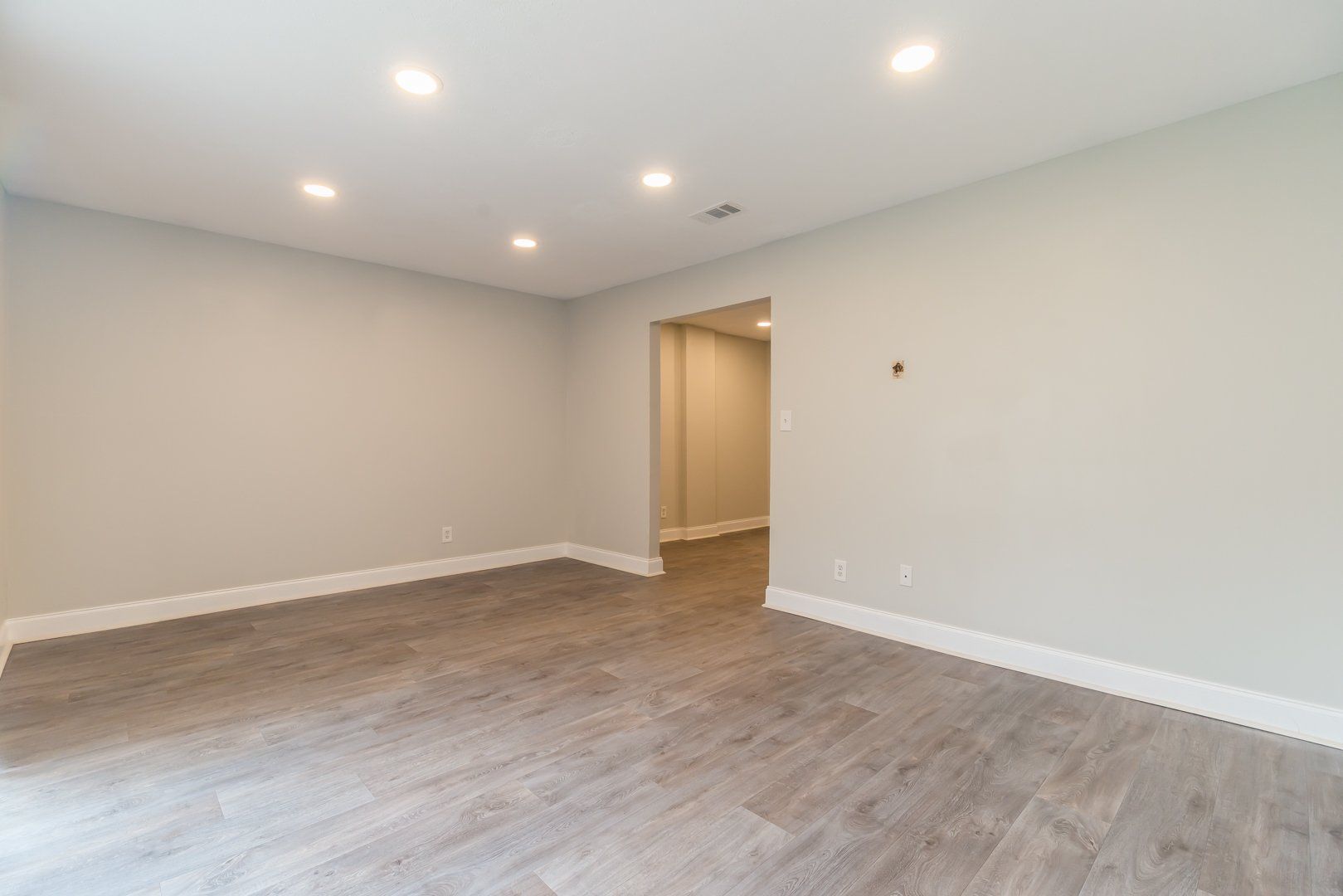 Empty modern room with recessed lights, wood-look flooring, and an open doorway.