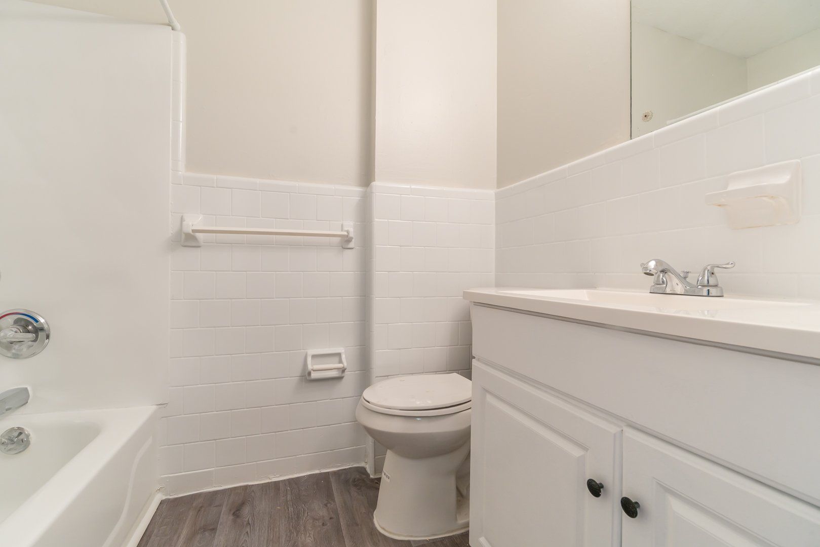 Bright bathroom with white sink, toilet, tub, and tile walls, shown from a corner view