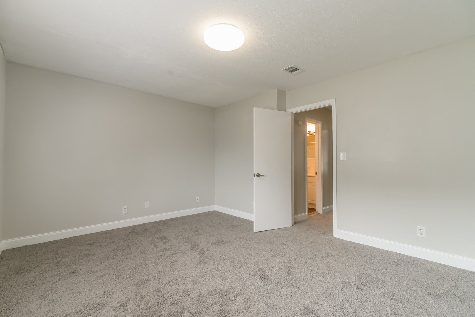 Empty carpeted bedroom with open door and bathroom light visible