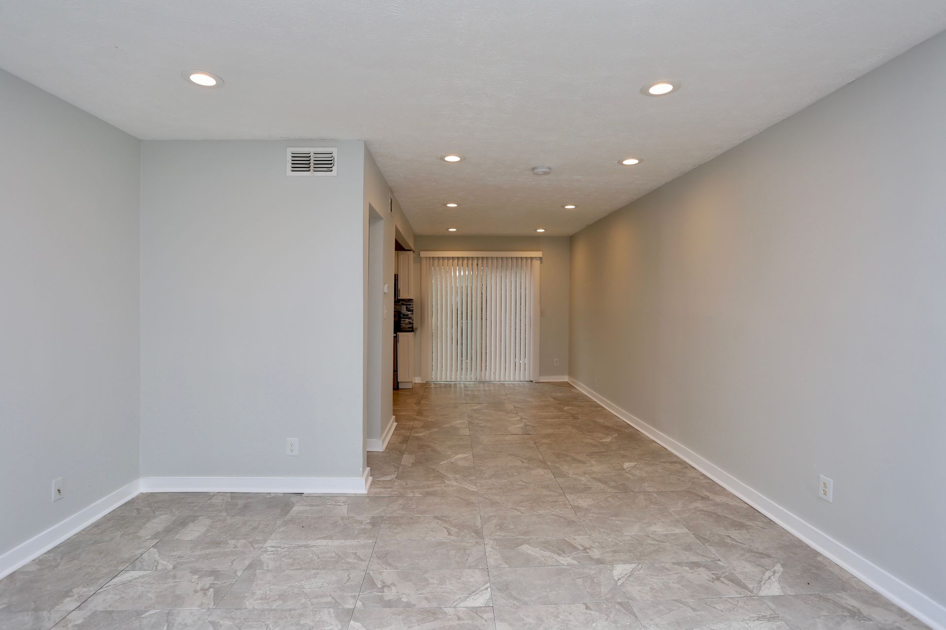 Empty modern hallway with light gray walls, tiled floor, recessed ceiling lights, and sheer curtains at the far end