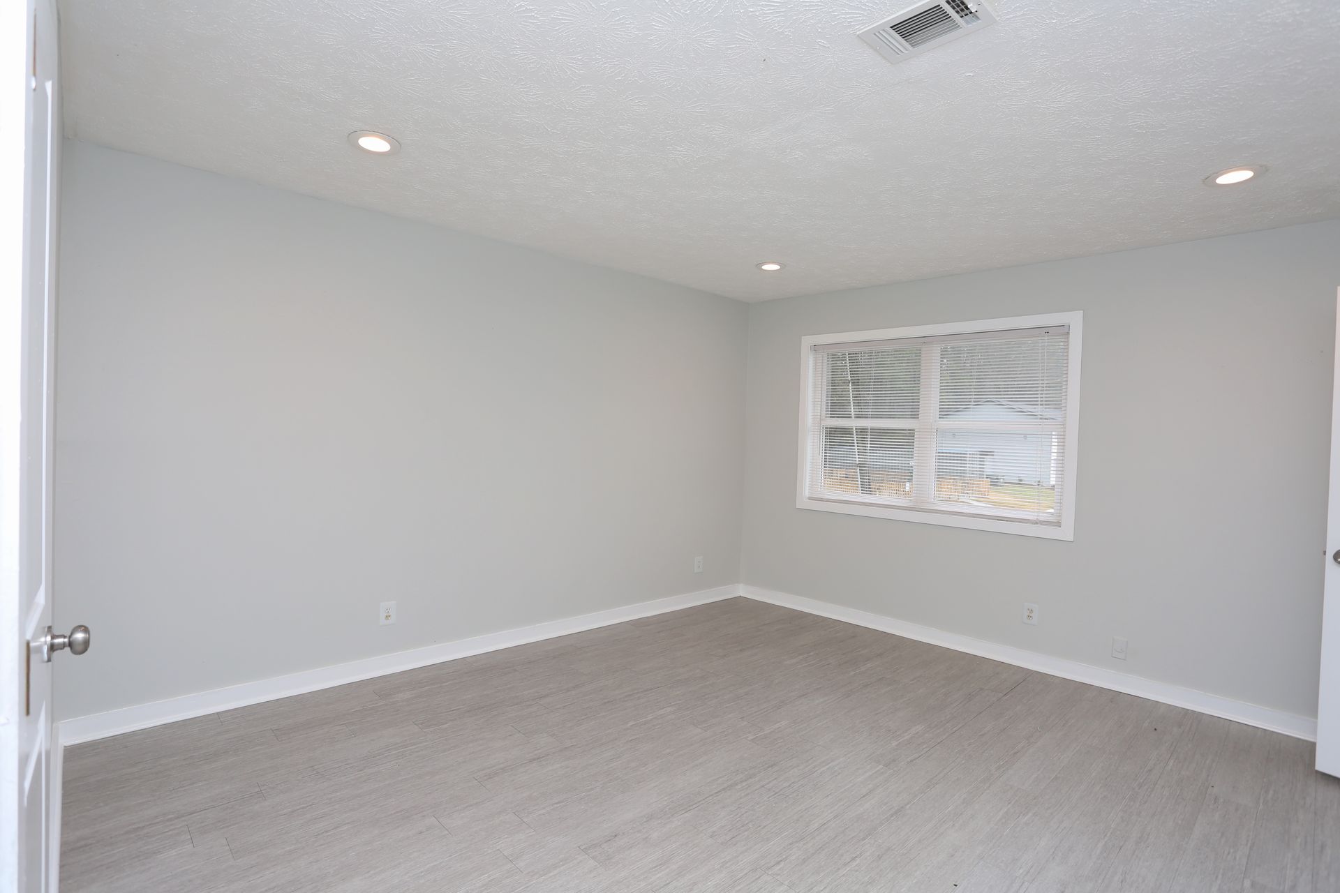 Empty light gray bedroom with beige carpet, white ceiling, and a window with blinds.