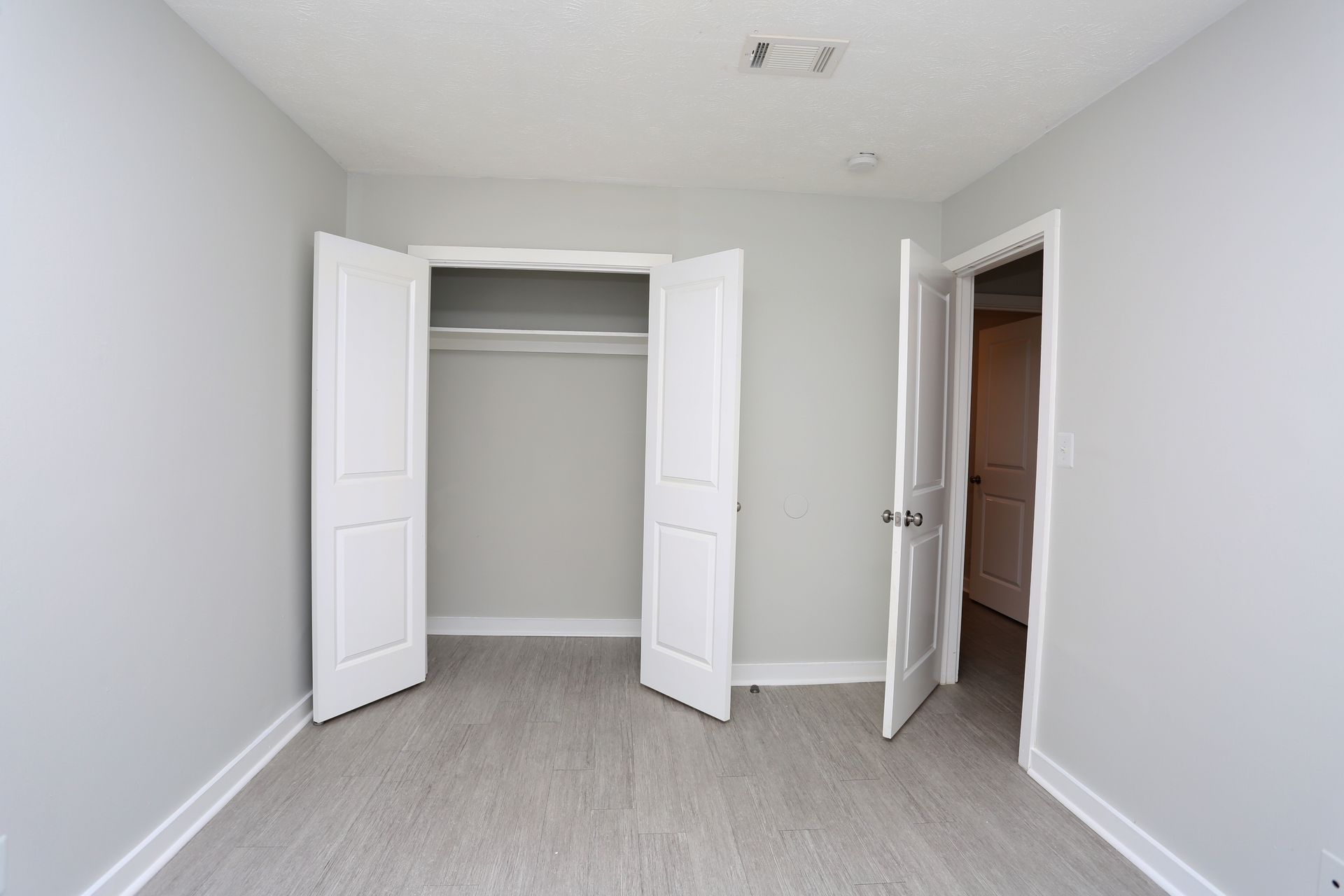 Empty white bedroom with open closet doors and an open doorway to a hallway