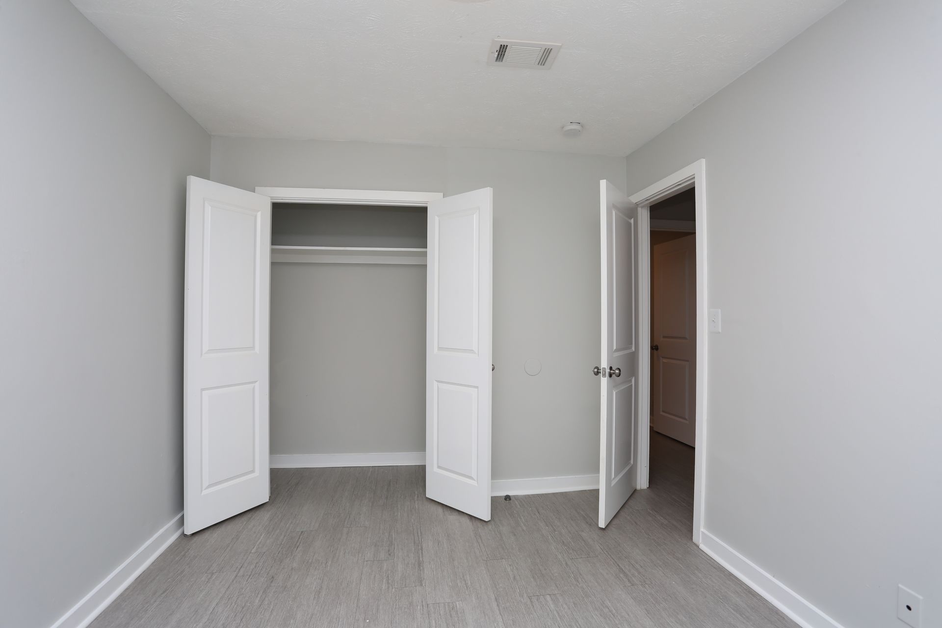 Empty white bedroom with open closet and adjoining door on carpeted floor