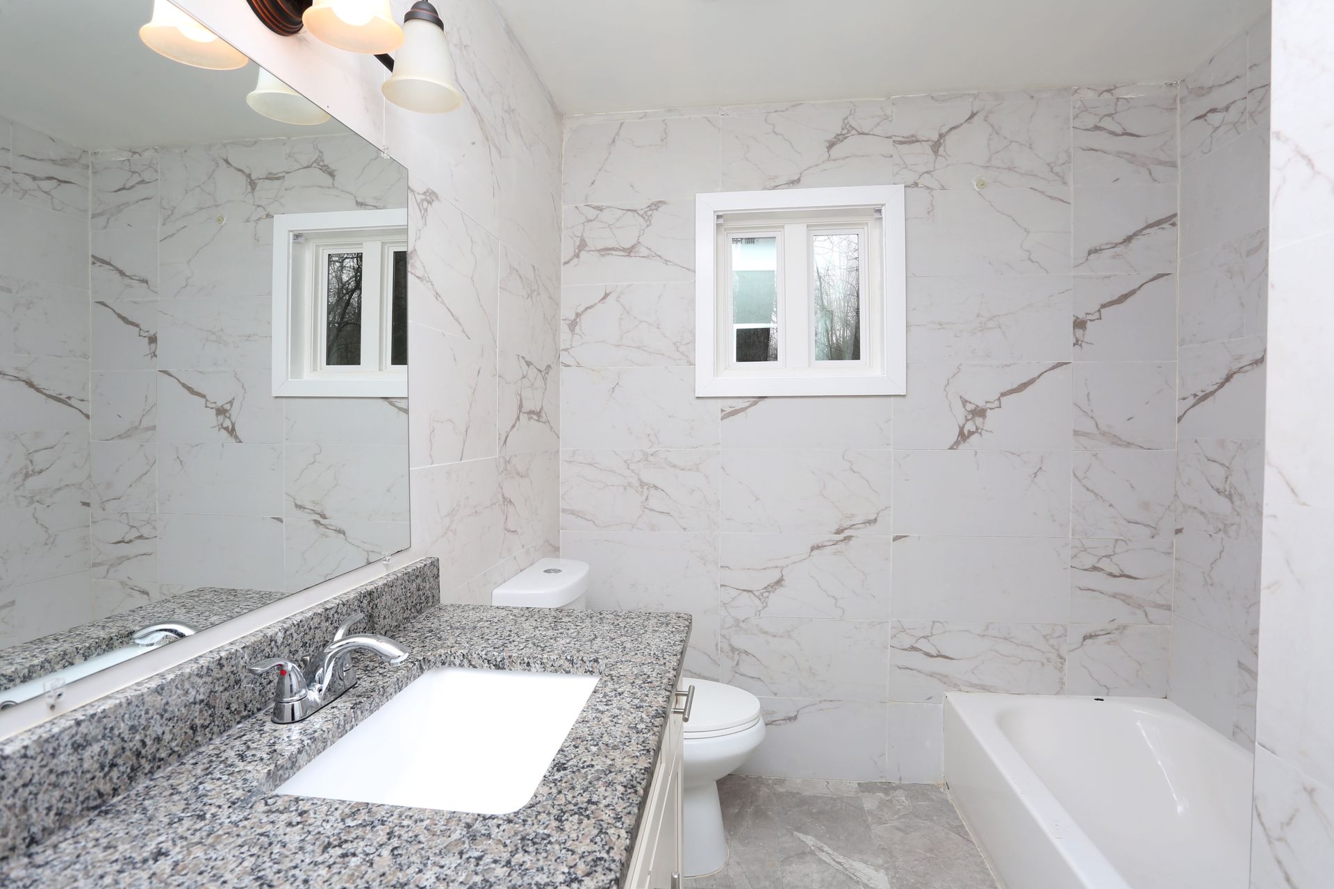 Bright marble bathroom with granite vanity, sink, mirror, toilet, and bathtub.