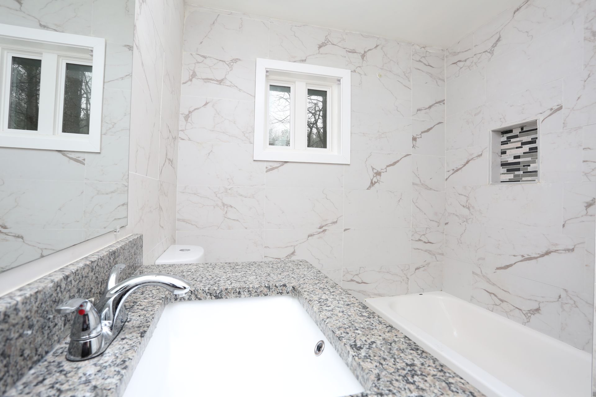 Bright white marble bathroom with double sinks, chrome faucets, and small windows above the vanity.