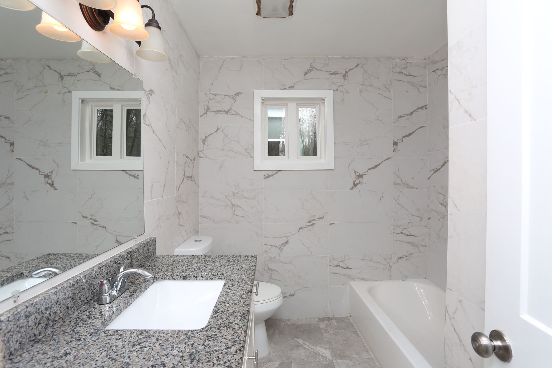 Modern white marble bathroom with granite vanity, mirror, window, and bathtub