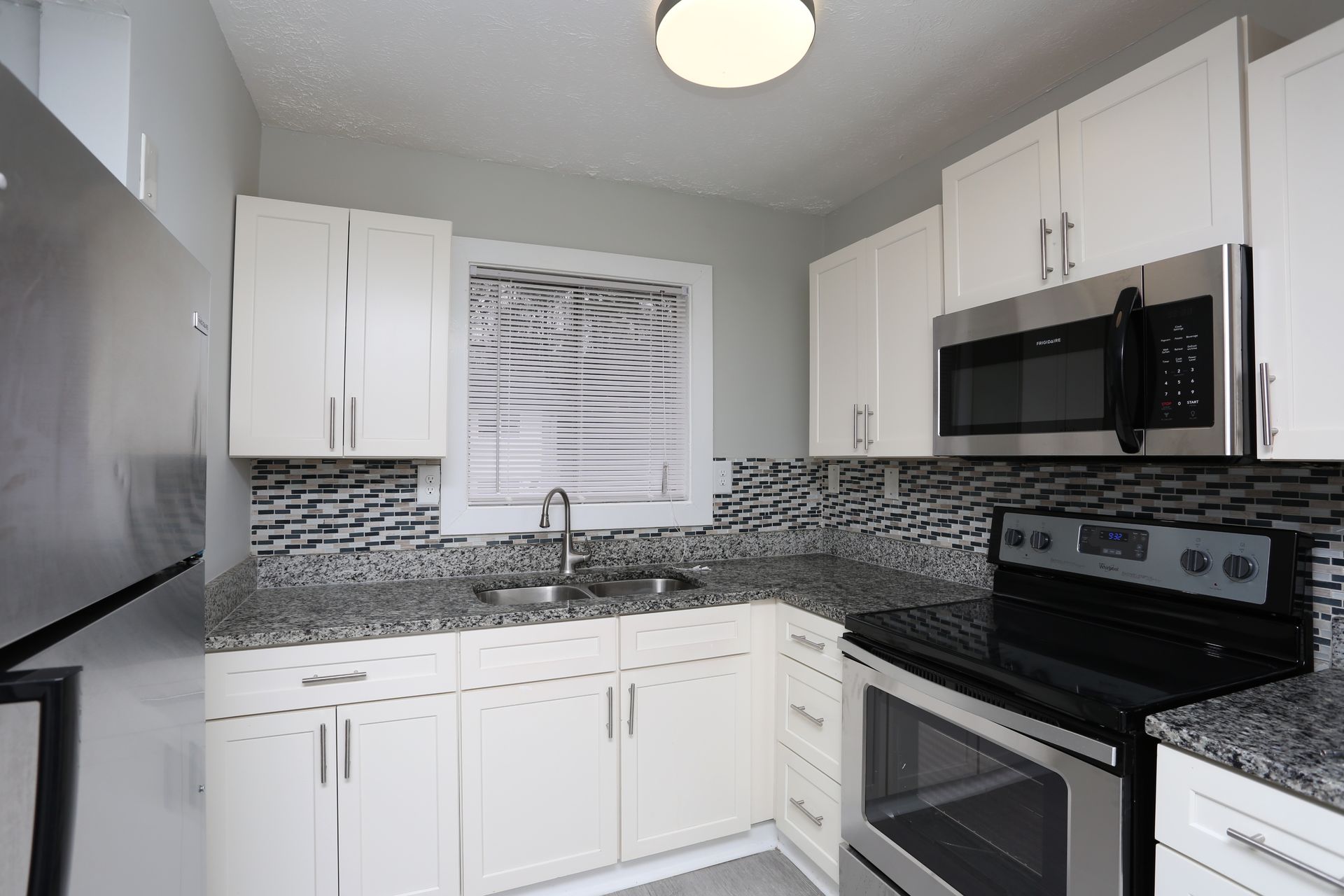 Bright modern kitchen with white cabinets, black appliances, gray tile backsplash, and stainless steel sink