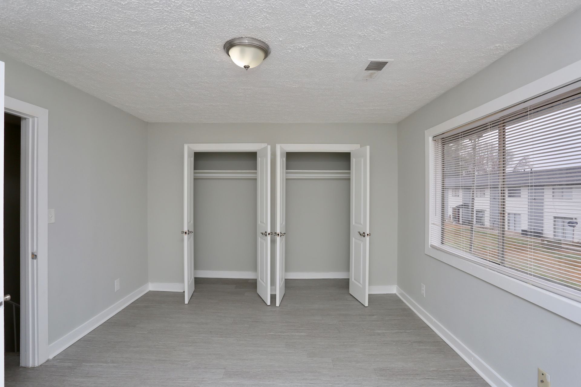 Empty bedroom with gray walls, white closet doors, and a large window with blinds.