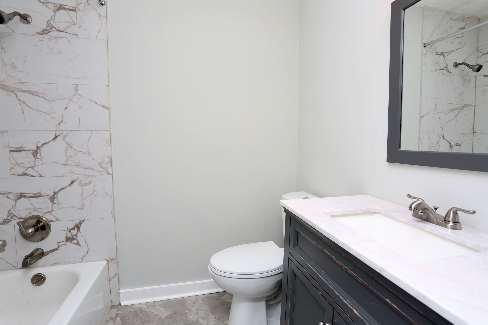 Small bathroom with white tiled tub, toilet, and dark vanity with mirror.