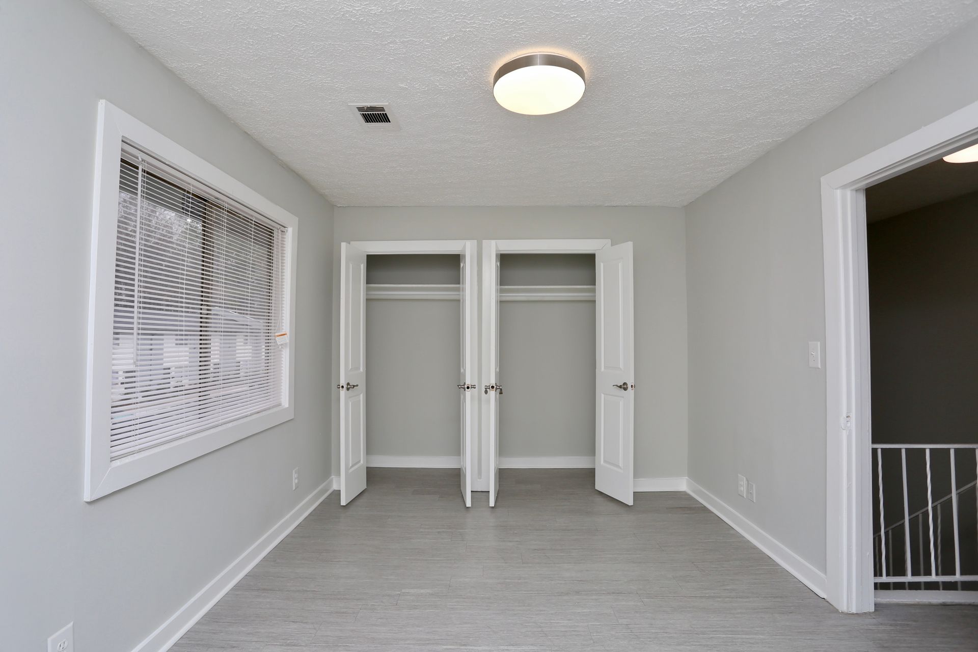 Empty gray bedroom with open closet, white trim, and a window with blinds