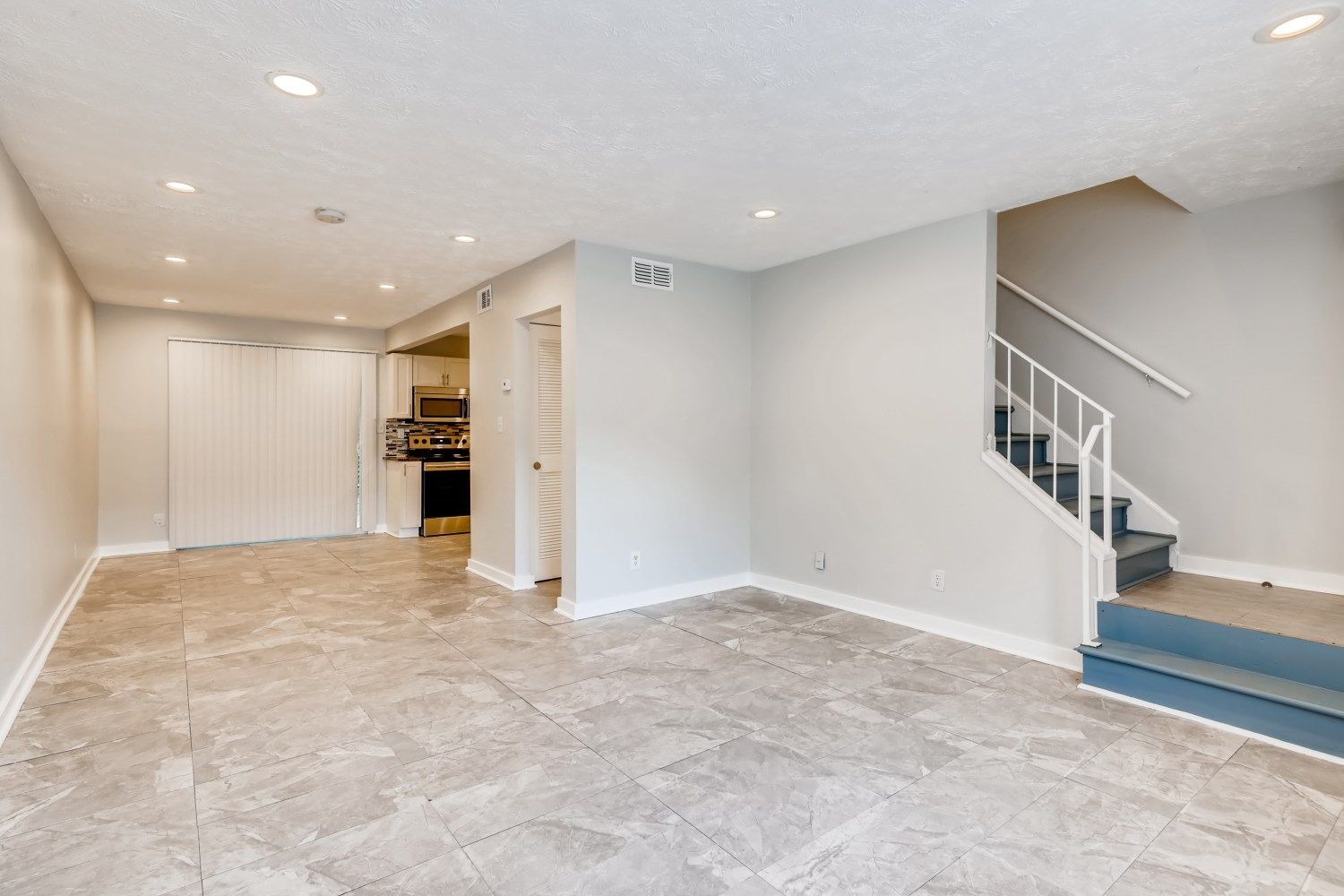 Empty tiled living room with white walls, recessed lights, and a staircase on the right