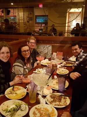 Group of friends smiling around a restaurant table with drinks and plates of food