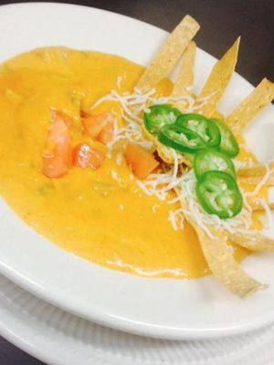 Bowl of creamy yellow soup topped with tortilla strips, jalapeños, shredded cheese, and diced tomatoes