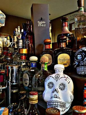 A shelf crowded with liquor bottles and a decorative sugar skull in front.