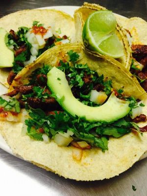 Three tacos topped with avocado, cilantro, and lime wedges on a plate