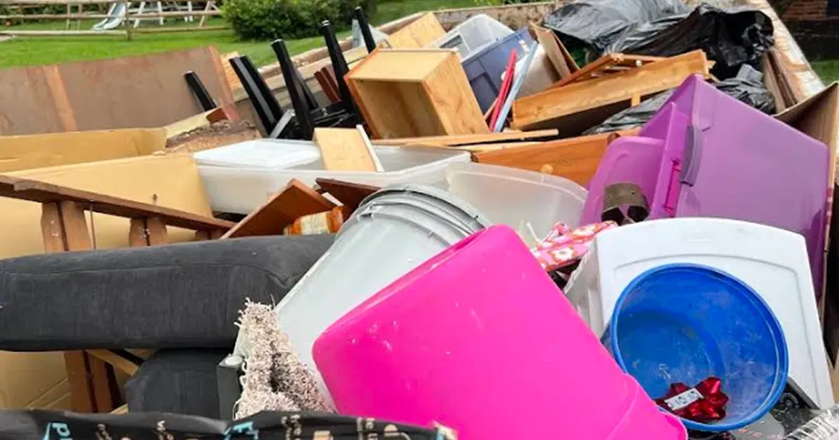 Overflowing dumpster with scattered furniture, boxes, and a bright pink bucket of debris