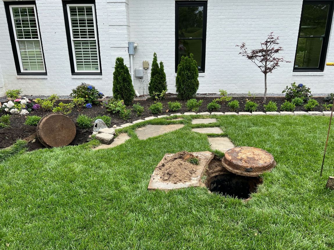 Backyard lawn with stepping stones, landscaped flower bed, and two tree stumps by a white house