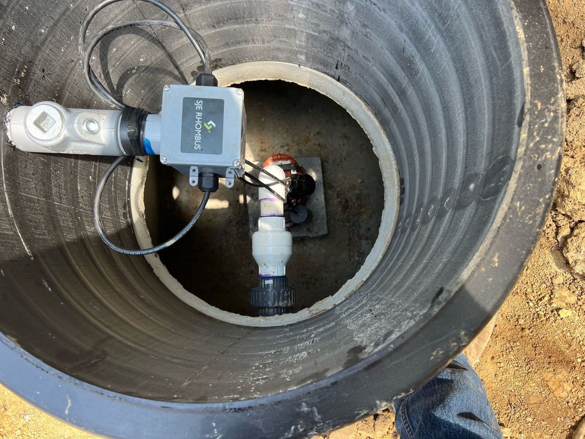 Water meter assembly inside a round underground manhole with pipes and a gray valve box attached