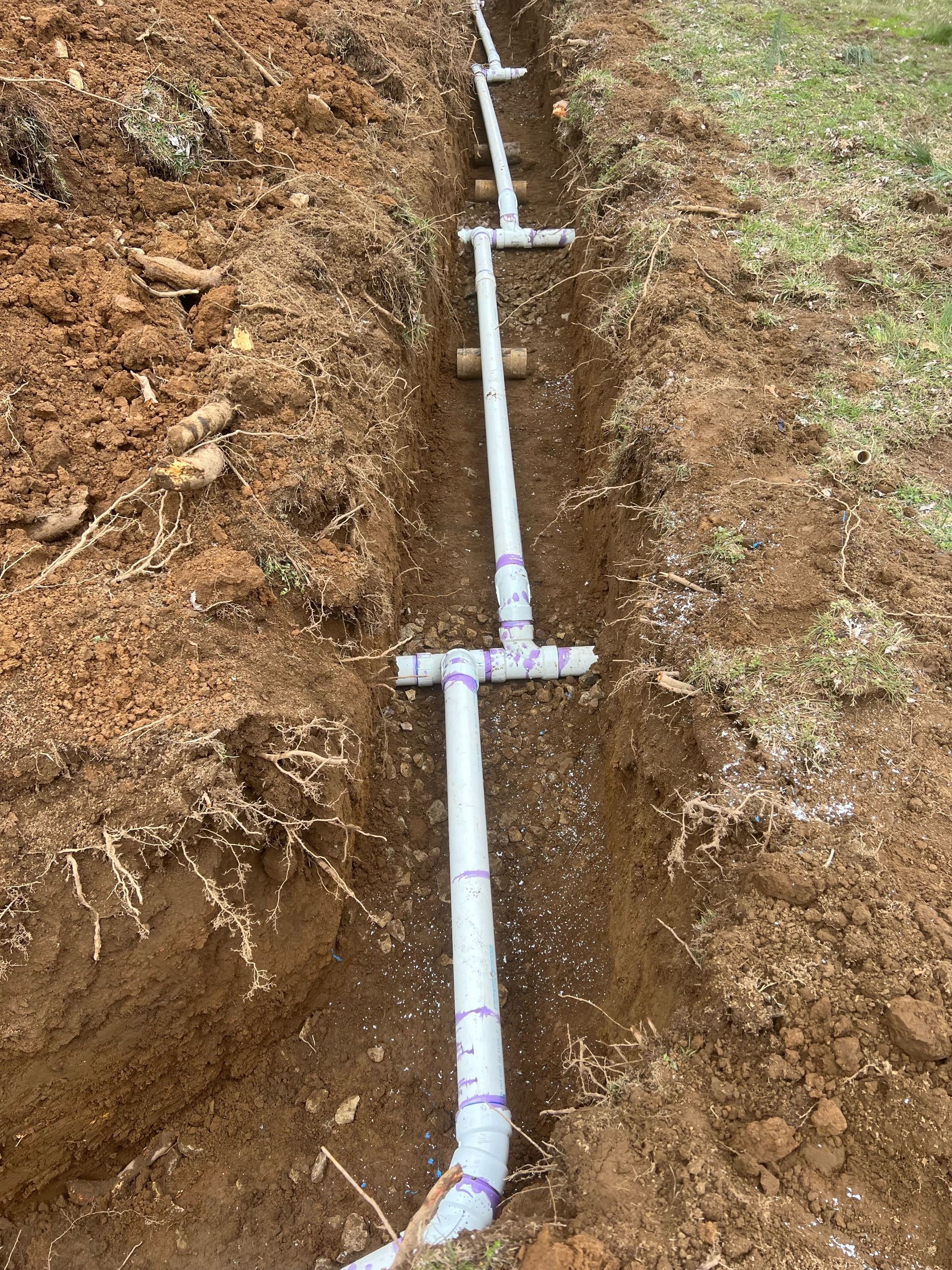 PVC pipe and fittings running through a narrow trench in brown soil