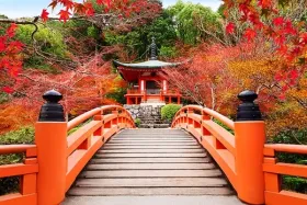 Traditional Japanese temple beyond an orange bridge surrounded by vibrant autumn foliage.
