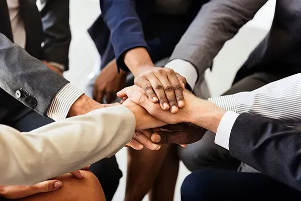 Team members placing their hands together in a stack, symbolizing collaboration and unity.