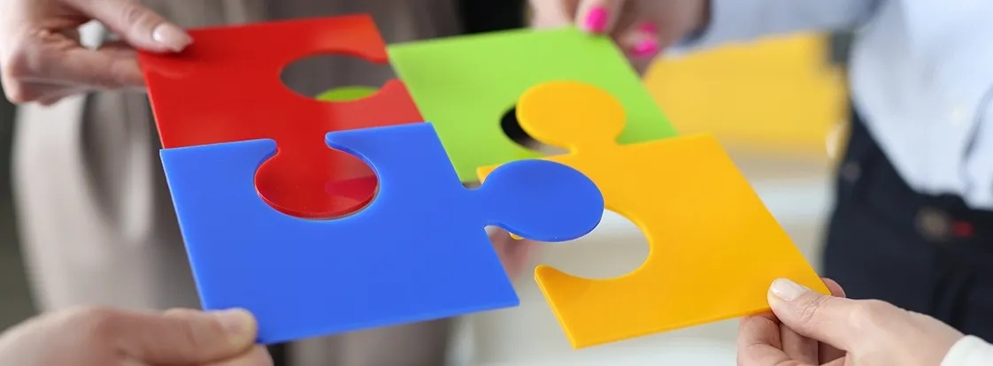 Hands holding colorful interlocking puzzle pieces coming together to form a complete picture.