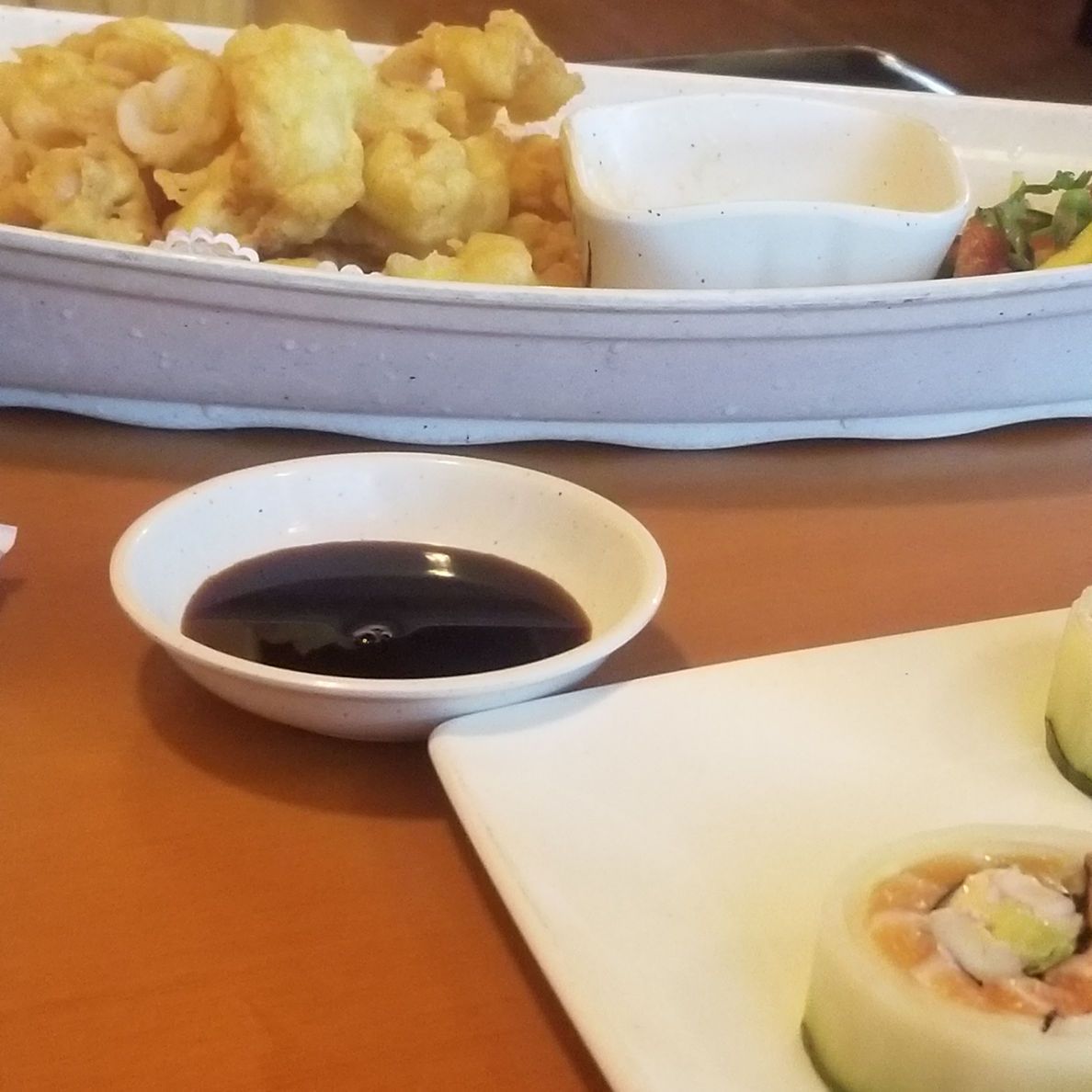 Plates of fried food and sushi with soy sauce on a restaurant table