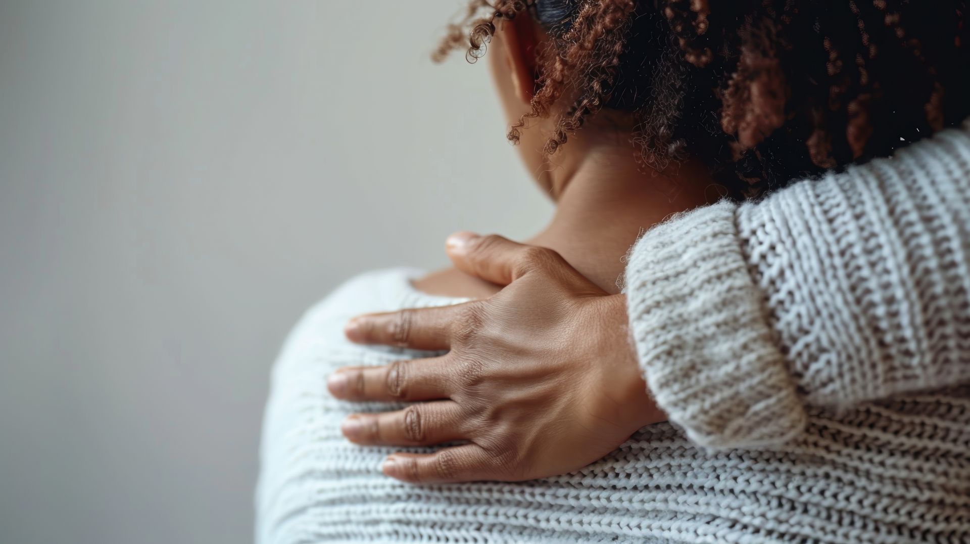 Hand resting on a person’s shoulder in a soft, comforting gesture against a neutral background