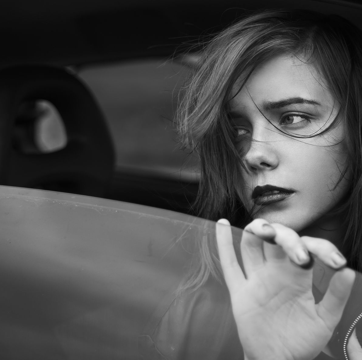 Black-and-white portrait of a woman looking out a car window with wind in her hair