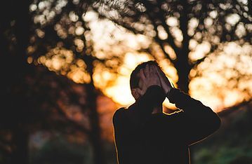 Silhouetted person holding their head against a glowing sunset in a wooded area